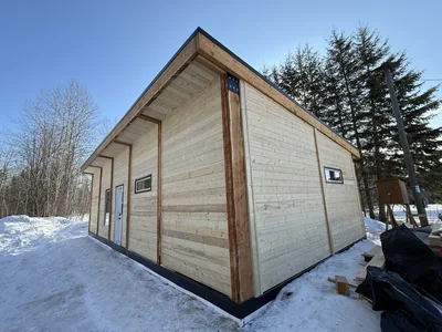 Timber-clad building in winter with deep roof overhangs, exposed wood posts, and black trim