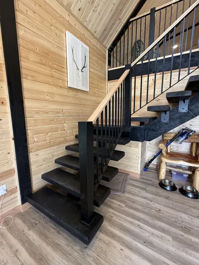 Open-riser black timber staircase with black railings, natural wood handrail, and timber-finished walls
