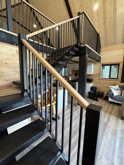 Open timber staircase with black railings leading to a loft above a finished timber living area