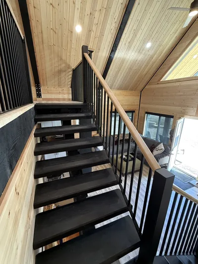 Open-riser staircase with black railings and natural wood handrail inside a timber-finished home