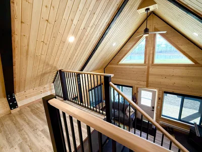 Finished timber loft with black railings, natural wood handrails, vaulted ceiling, and triangular windows overlooking the main floor