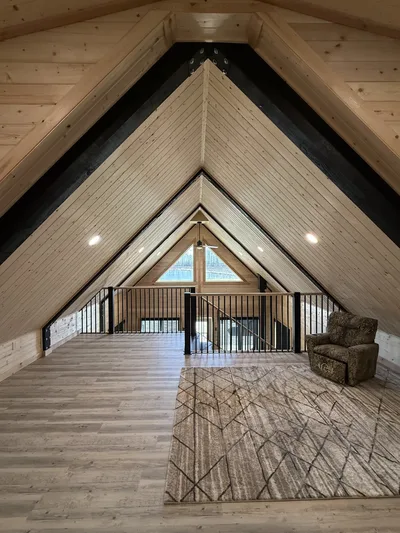 Wide finished timber loft beneath a dramatic vaulted wood ceiling with black structural beams and railing overlooking the main floor
