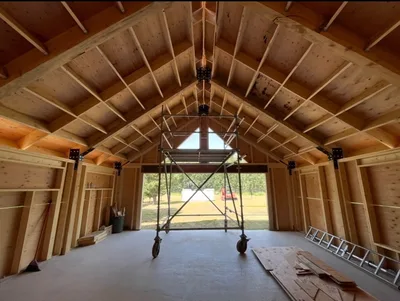 Symmetrical interior construction view of a vaulted timber structure with exposed roof framing, black connectors, and rolling scaffold