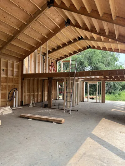 Interior construction view showing an open loft, exposed timber roof framing, structural beams, and framed walls