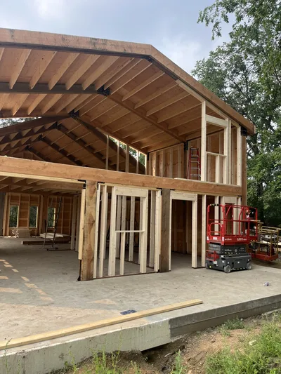 Two-storey timber home under construction with exposed structural beams, loft framing, wall framing, and lift equipment