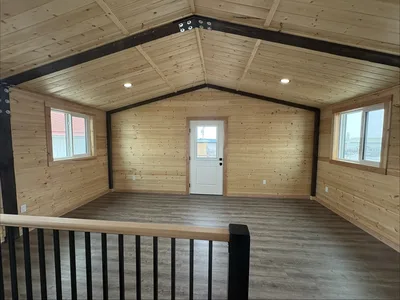 Finished open timber loft with black structural beams, wood ceiling and walls, windows, and dark flooring