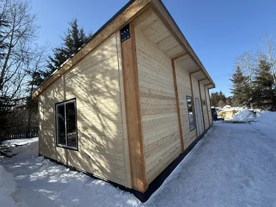 Winter view of a timber-clad building corner with exposed wood posts, black trim, and narrow windows