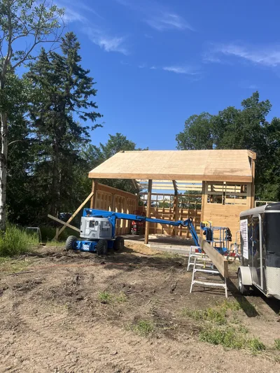 Timber home under construction with roof sheathing underway, framed walls, lift equipment, and exposed beams