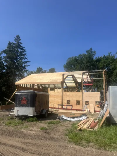 Timber home framing in progress with exposed roof structure and a Timber Built Homes trailer in the foreground