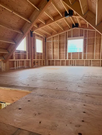 Unfinished loft interior showing timber beams, roof framing, wall studs, and plywood subfloor