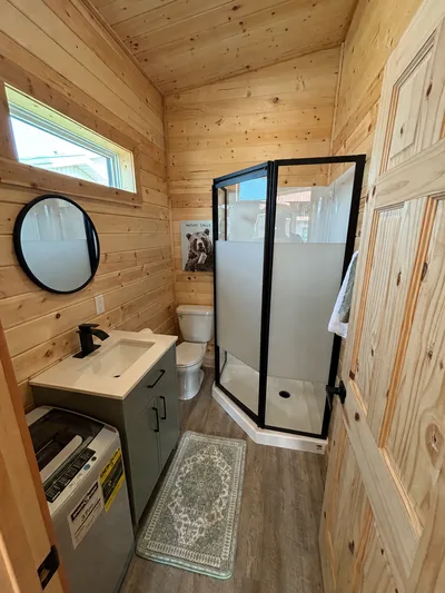 Compact finished bathroom with timber walls, black-framed shower, vanity, mirror, and high window