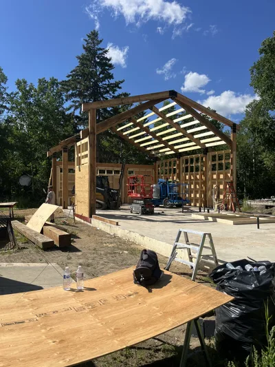 Timber home under construction with large posts and beams, roof framing, and framed walls under a blue sky