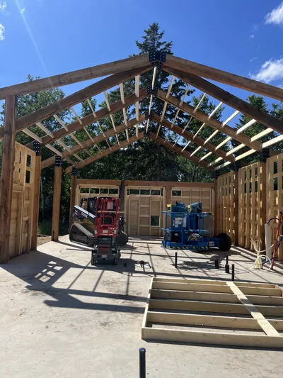 Interior construction view looking through a symmetrical timber roof structure with exposed beams and framed walls