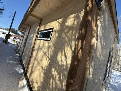 Close exterior view of timber siding, an exposed wood post, narrow window, and roof overhang