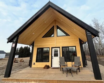 Timber home with natural wood siding, black structural accents, triangular windows, and a covered front deck