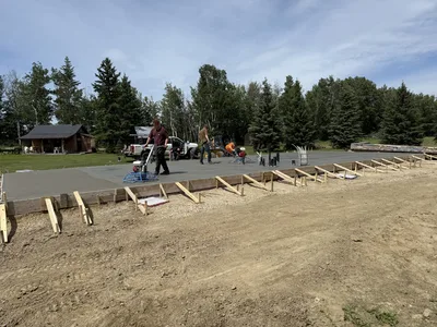 Crew finishing a large concrete slab foundation surrounded by formwork on a rural building site