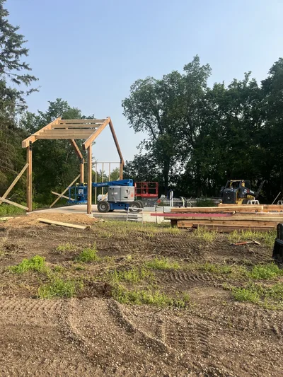 Early timber frame construction with the first large posts, beams, and roof members standing on a concrete slab