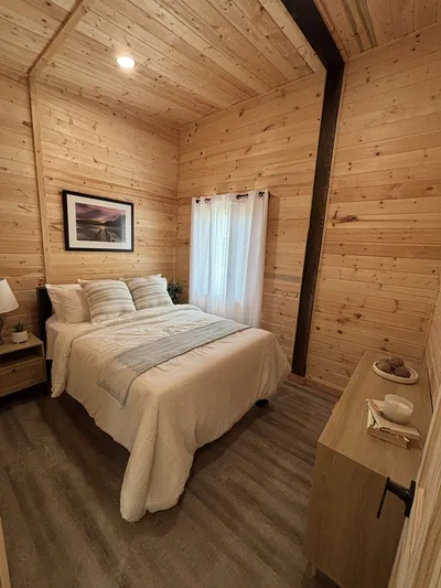 Finished bedroom with timber walls and ceiling, dark structural beam, neutral bedding, and dark plank flooring
