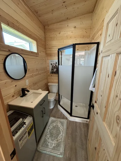 Compact finished bathroom with timber walls, black-framed shower, vanity, mirror, and high window