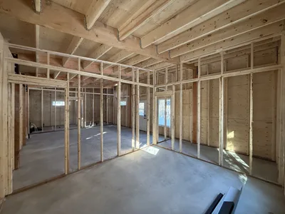 Interior construction view showing framed partition walls beneath exposed timber beams and roof framing