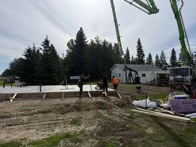 Concrete pump boom silhouetted against the sky while a crew works on a slab foundation below