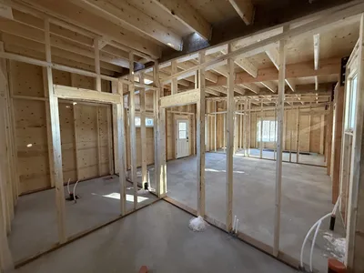 Interior construction view showing framed rooms, exposed roof framing, and timber structural members