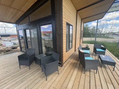 Covered timber deck with black structural posts, large glass doors, wood decking, and outdoor seating