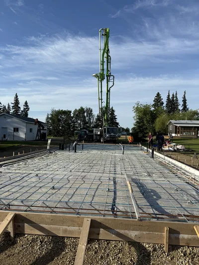 Prepared slab foundation with reinforcing steel, embedded lines, and a concrete pump positioned beyond the formwork