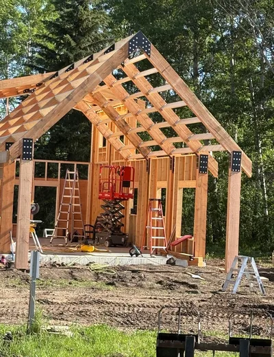 Gable timber structure under construction with exposed posts, beams, roof framing, and framed walls