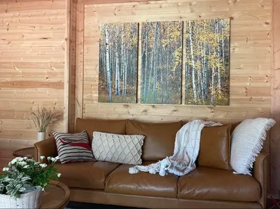 Warm timber living room with leather sofa, textured pillows, coffee table flowers, and woodland artwork