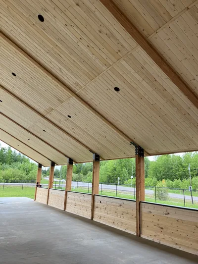 Interior of an open timber pavilion with exposed posts, wood ceiling, half-height wood walls, and concrete floor