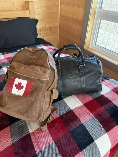 Backpack and duffel bag resting on a plaid bedspread beside a wood wall and window