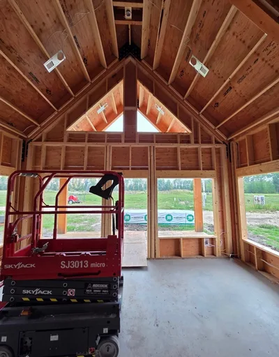 Interior construction view of a vaulted timber ceiling with framed gable wall, exposed roof structure, and lift equipment