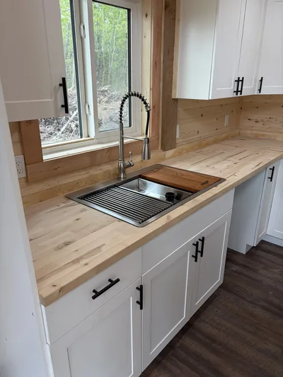 Timber kitchen with white cabinets, black hardware, wood countertops, stainless sink, and pull-down faucet beneath a window