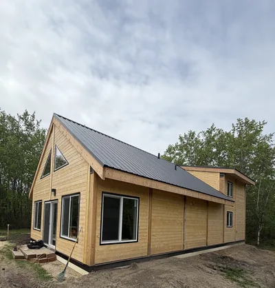 Completed timber home with natural wood siding, dark metal roof, black window trim, and mixed gable and low-slope roof forms