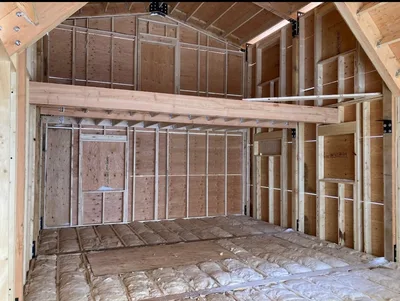 Interior construction view of an open loft with exposed timber beams, roof framing, and framed walls