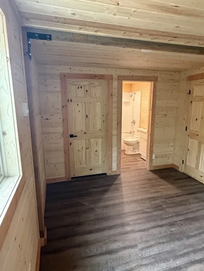 Finished timber interior with natural wood doors and walls, dark plank flooring, and a bathroom visible through an open doorway