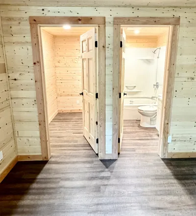Timber-finished interior with two natural wood doorways, one opening into a bright bathroom with tub and vanity
