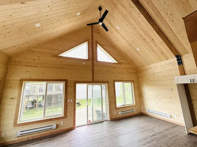 Finished vaulted timber great room with triangular clerestory windows, black ceiling fan, wood walls, and large windows