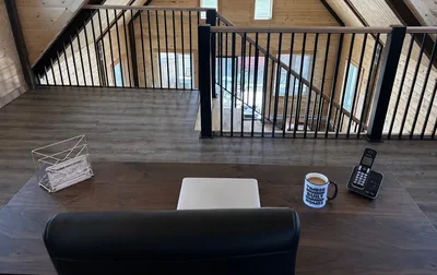 Timber loft office desk overlooking black railings and the open interior below, with branded Timber Built Homes mug