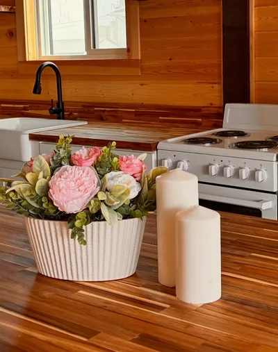 Kitchen detail with warm wood countertop, white stove, black faucet, flowers, candles, and timber wall finish