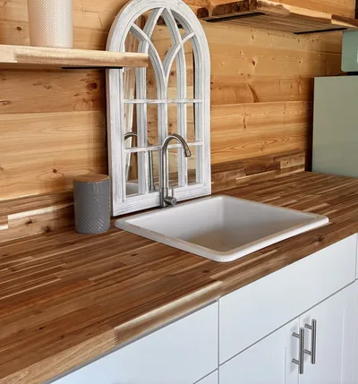 Close kitchen detail with white sink, wood countertop, decorative mirror, and timber wall finish