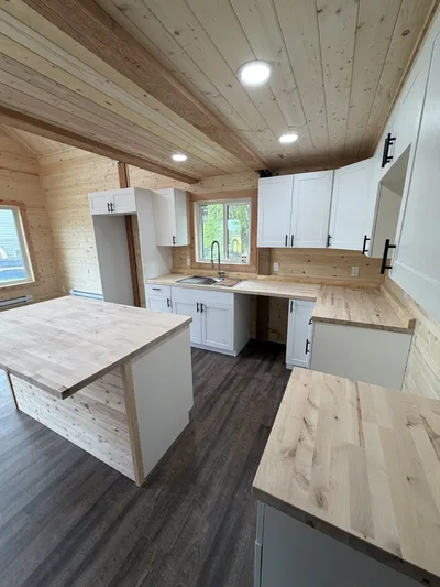 Finished timber kitchen with white cabinets, black hardware, wood countertops, island, and dark plank flooring